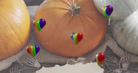 Showing large orange pumpkin resting on burlap on wood, with rainbow-heart balloons, skeleton hands