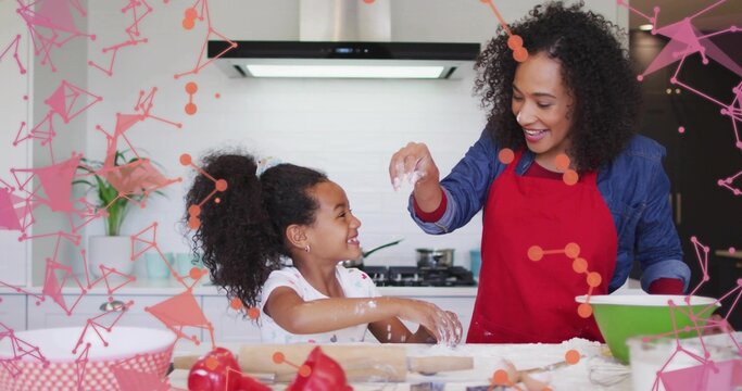 Sprinkling woman in red apron guiding daughter in home kitchen, with rolling pin and green bowl