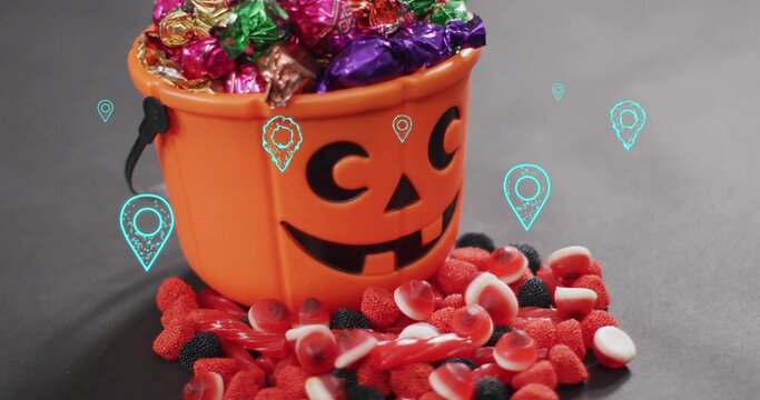 Showing pumpkin bucket holding foil candies on dark tabletop, red gummies and turquoise pins
