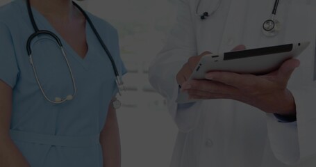 Reading two clinic staff consulting on tablet in clinic, showing stethoscopes lab coat and scrubs