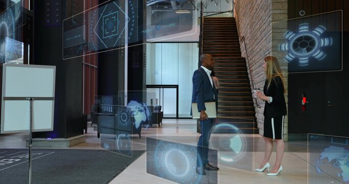 Talking coworkers wearing business suits holding laptop and tablet in office lobby, with holograms
