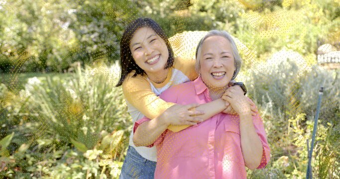 Hugging daughter holding mother in sunny garden, wearing casual clothes with smartwatch necklace - Powered by Adobe