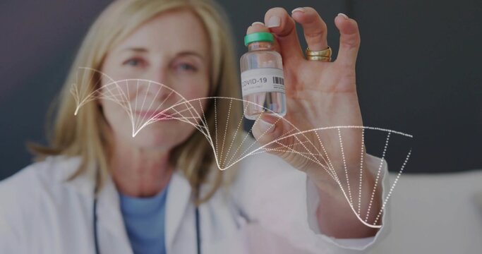 Senior female doctor holding COVID-19 vial in clinic, with white lab coat and DNA helix overlay - Powered by Adobe