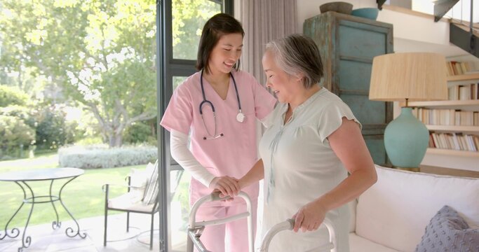 Supporting caregiver in pink scrubs placing hand on senior using walker at home with stethoscope