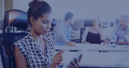 Tapping adult woman using tablet in office, wearing patterned blouse and bun, seated in mesh chair