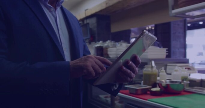 Tapping man in dark blazer checking tablet at kitchen prep counter, green cutting board present