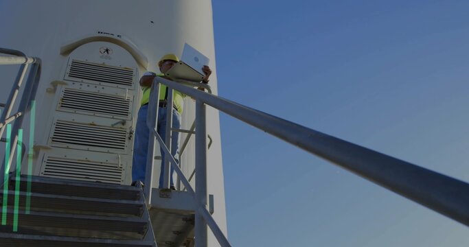Standing turbine tech in hard hat and hi-vis vest leaning on railing with laptop, copy space
