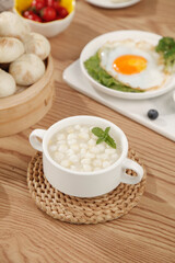Delicious Asian breakfast with corn soup, xiao long bao and fried egg on rustic wooden table