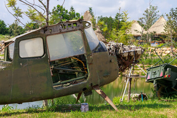 Abandoned Military Helicopter Wreckage and Engine on Display Near Thatched Huts