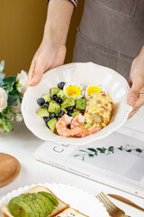 Healthy Salad Bowl with Shrimp Avocado and Boiled Eggs Served by Hand on White Table