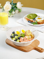 Healthy shrimp avocado salad bowl with eggs corn blueberries on wooden board breakfast lunch meal