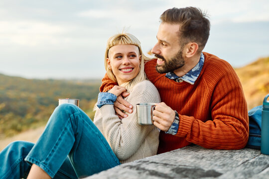 Hiking couple  enjoys nature  taking a break with water bottle or hot drink tea at the table  in a lush forest during a sunny day