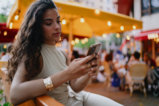 Focused woman types on smartphone at outdoor cafe, embodying mobile productivity, tech-savvy lifestyle, and the flexibility of digital-age communication. - Powered by Adobe