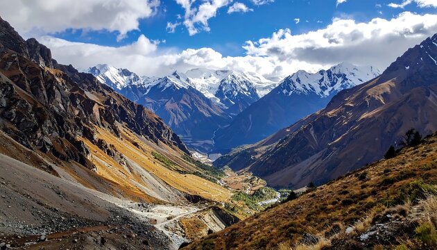 Majestic mountain valley with snow-capped peaks and autumn foliage under a partly cloudy blue sky - Powered by Adobe