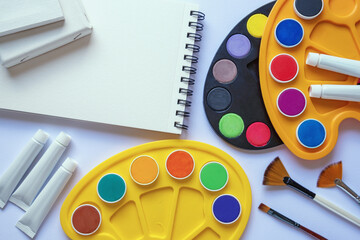 Bright watercolor paints, paint tubes, palettes, paintbrushes and sketchbook. Free space for text or image