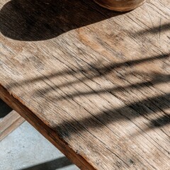 Rustic wooden table surface in sunlight, close-up shot with shadows, texture and grain detail, natural light, weathered finish
