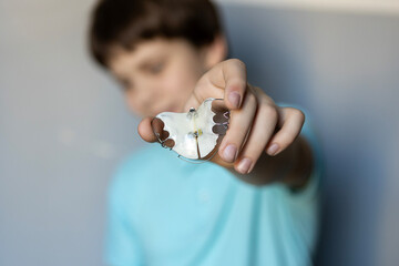Young child holds clear dental retainer in hand while sitting against a light blue wall in a cozy indoor setting