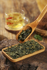Dried Mulberry Leaves Tea with Wooden Spoon and Cup on Natural Bark Surface