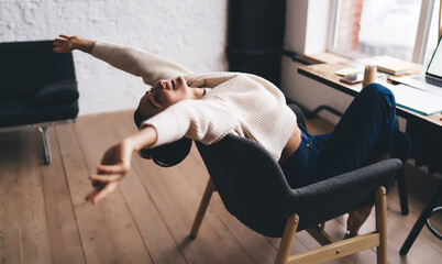 Remote freelancer stretches back in chair after digital brainstorming session, embodying...
