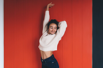 Young woman stretching with closed eyes against red wall, expressing calm, self-love and morning...