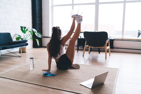 Woman extends leg high while following a virtual trainer on her laptop, showcasing digital guided flexibility and strength with smart workout synergy.