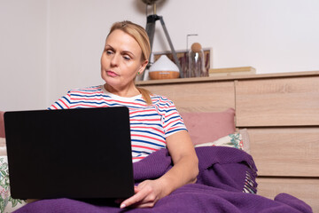 Mature woman sitting on couch with laptop, working remotely or studying online at home. Concept of digital lifestyle, communication, education, and technology use for seniors.
