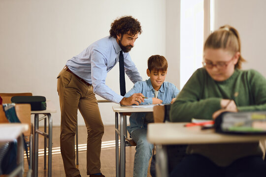 Young male professor assisting elementary schoolboy on a class at school.