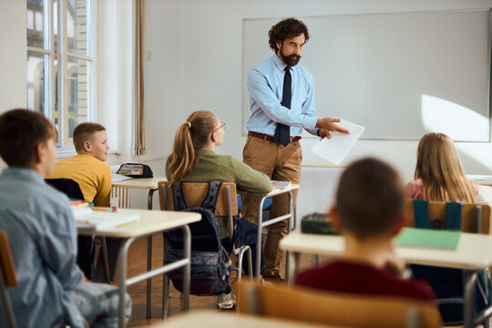 Young happy teacher talking to elementary students on a class in the classroom