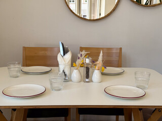 Minimalist table setting with plates and dried flowers near wall mirrors. Natural light, Scandinavian design, and serene dining mood.
