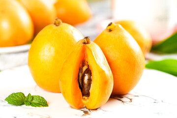 Fresh Ripe Loquat Fruits Cut in Half Showing Seed on White Marble Surface with Mint Leaves