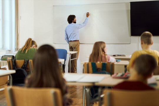 Mid adult  teacher teaching elementary students on a class in the classroom and writing on whiteboard. 
