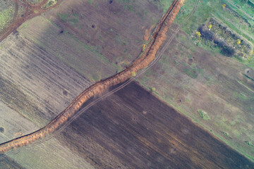 Aerial photo capturing a defensive trench line winding through agricultural fields in autumn colors, showcasing contrasting textures of soil, grass, and farmland from a top view