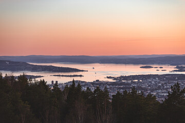 Soft pastel sunset over Oslofjord with islands, calm water and forested hills, reflecting the gentle Scandinavian evening mood and golden serenity