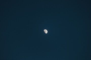 Bright half moon floats above Oslo, Norway, surrounded by deep blue night sky, capturing northern serenity and minimal Scandinavian atmosphere