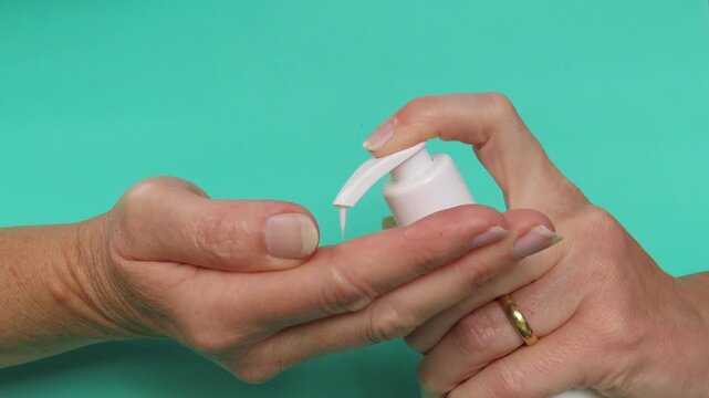 Video closeup of woman hands pouring cosmetic product in hands and gently spreading it. Turquoise background. Hands applying cream. Skin care routine.