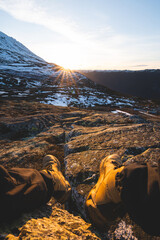 Golden sunset over the snowy slopes of Gaustatoppen Mountain in Norway, captured from rocky terrain with hiking boots in frame