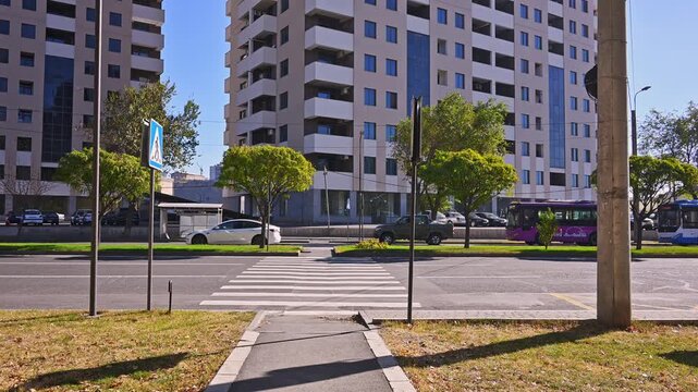 A street with a crosswalk and a bus stop. The street is empty and the buildings are tall