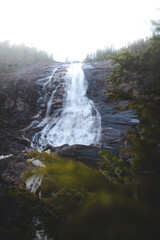 Powerful Reiarsfossen waterfall near Setesdal Valley, Norway. Water cascades over dark cliffs surrounded by pine forest, symbol of wild Nordic nature
