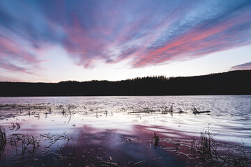 Soft pastel clouds reflect in calm lake water during sunset in Setesdal Valley, Norway. Peaceful Scandinavian evening atmosphere full of serenity and natural beauty