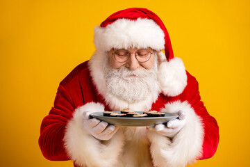 Santa Claus holds a plate of cookies and smiles warmly in a bright yellow studio celebrating Christmas joy and family moments