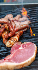 grilling beef steak, chicken drumsticks and sausages on the barbeque outdoors at a picnic