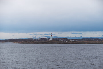 Lonely lighthouse standing on the rocky coast near Kristiansand, Norway. Calm Scandinavian seascape under a moody sky capturing the spirit of coastal solitude.