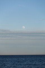 Full moon rising over the calm waters of the North Sea near Skagen, Denmark. Minimalist Scandinavian seascape bathed in soft blue light