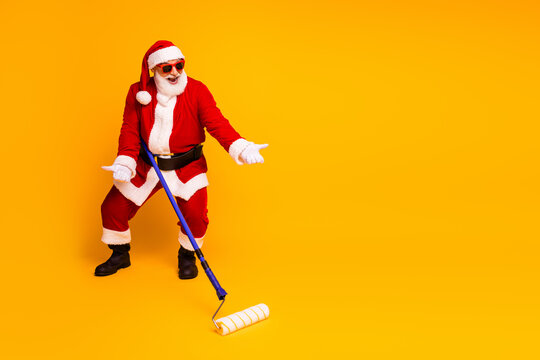 Santa in a red costume with a paint roller yellow backdrop ready for festive home improvement humor and Christmas marketing campaigns