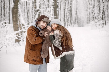 Young family with baby son on hands standing in winter forest