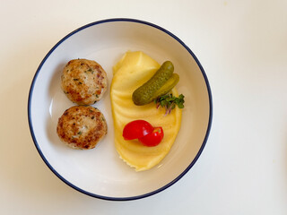 Top view homemade chicken patties with mashed potatoes, pickles, and cherry tomatoes. Simple comfort food, cozy lunch, and minimal serving style.