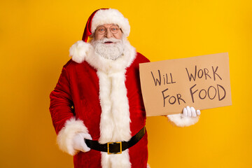 Santa Claus in red suit holds a cardboard sign will work for food against a bright yellow background celebrating christmas spirit