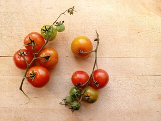 Top view of two clusters of colorful cherry tomatoes on the wooden board. Some tomatoes are still raw.