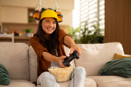 Woman playing video game wearing beer helmet and smiling - Powered by Adobe