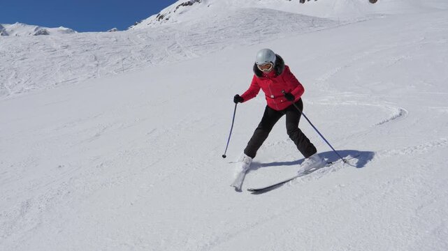 Beginner skier in sport helmet learns to ski using snowplow technique on snow mountain slope. Novice going down well groomed slope in mountain resort. Glides slowly braking with ski edges